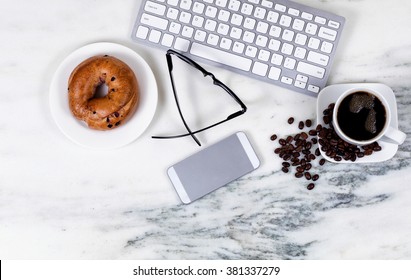 Overhead view marble kitchen counter top with computer keyboard, cell phone, reading glasses, dark coffee, beans and bagel on plate. Work at home concept.  - Powered by Shutterstock