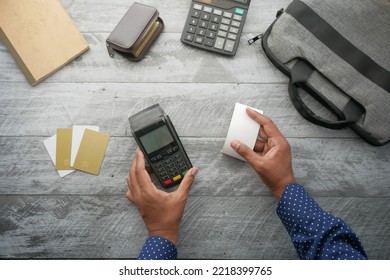 Overhead View Of Men Holding POS Machine And Long Roll Paper On Table 