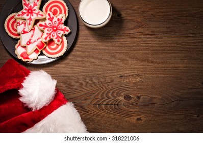 Overhead View Of Milk, Christmas Cookies And A Santa Hat On A Wooden Background.