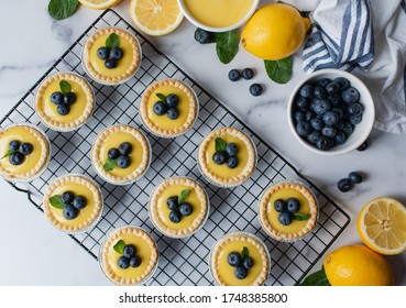 Overhead View Of Mini Lemon Tarts With Blueberries On Marble Counter.