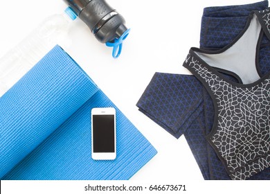 Overhead View Of Mobile Device, Yoga Mat, Yoga Clothing And Bottle Of Water On White Background