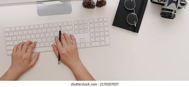 Overhead view, Modern minimal workspace office desk with a female's hands typing on computer keyboard, camera, eyeglasses and stuff on white table background. 3d rendering, 3d illustration
