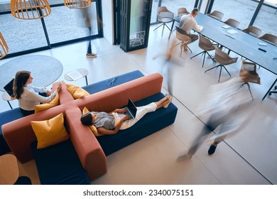 Overhead View Of Modern Open Plan Office With Staff Working Around Table And Breakout Seating Area