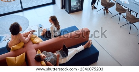 Overhead View Of Modern Open Plan Office With Female Staff Working In Breakout Seating Area