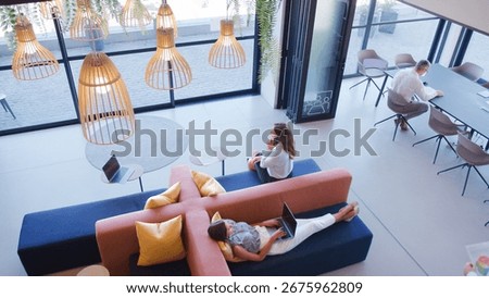 Overhead View Of Modern Open Plan Office With Staff Working Around Table And Breakout Seating Area