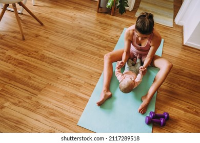 Overhead view of a mom working out with her baby on an exercise mat. Caring mom doing sit up exercises with her baby at home. New mom bonding with her baby during her post-natal fitness routine.