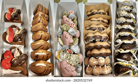 An overhead view of multiple rows of gourmet donuts and pastries dipped in dark chocolate with various colorful toppings including cream, berries and decorative designs, neatly arranged in a bakery box.
