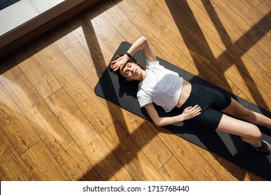 Overhead View Of Muscular Young Woman Lying On Exercise Mat. Relaxing After Workout At Gym.