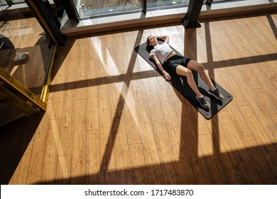 Overhead View Of Muscular Young Woman Lying On Exercise Mat. Relaxing After Workout At Gym.