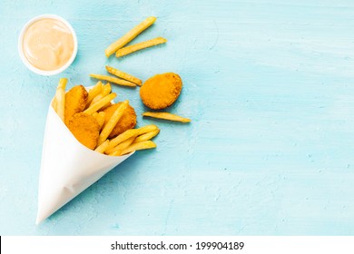 Overhead view on a blue background with copyspace of medallions of fried fish and chips in a takeaway paper cone with savory mayonnaise dip - Powered by Shutterstock