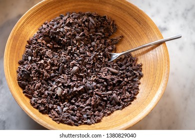 Overhead View On Cocoa Nibs In A Wooden Bowl, On A White Marble Counter, In A Chocolate Ingredient Background