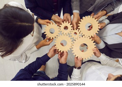 Overhead view on diverse business team people hands holding gear wheels finding working solutions. Power partnership, engineering teamwork, manage team work and company activities concept - Powered by Shutterstock