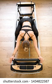 Overhead View On Individual Woman Doing Pilates Stretch On Reformer Bed Above Hardwood Floor