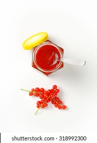 Overhead View Of Opened Jar With Yellow Lid, Filled With Fruit Jam And With Immersed Teaspoon Accompanied By Clusters Of Fresh Red Currant