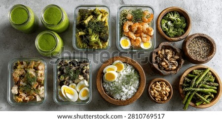 Overhead view of organized meal prep containers filled with healthy food options, alongside refreshing green smoothies.