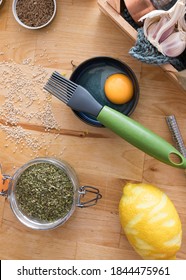 Overhead View Of A Pastry Brush On A Bowl With A Egg Yolk Inside In The Middle. Additional Spice Jars And A Grated Lemon Are Round It.