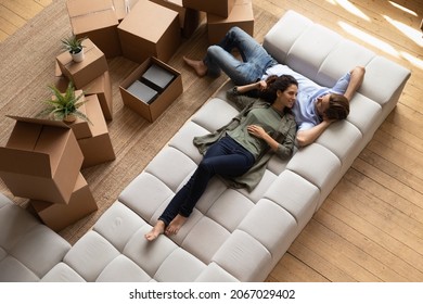 Overhead view peaceful young couple relaxing on fashionable cozy sofa near heap of packed belongings in cardboard boxes, resting at own house at relocation day. Bank loan and mortgage, tenancy concept - Shutterstock ID 2067029402