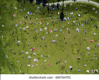 Overhead View Of People In A City Park On A Summer Day, Sitting, Standing, On Picnic Rugs,