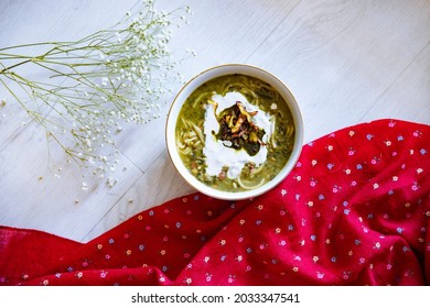 Overhead View Of Persian Pottage With White Flower And Red Fabric On White Wood Background