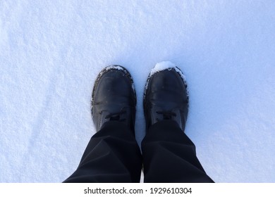 An Overhead View Of A Person In Black Pants And Black Leather Boots On The Snowy Road In Winter