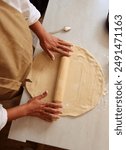 An overhead view of a person rolling out dough with a rolling pin on a marble countertop. The scene is set in a kitchen, conveying the concept of homemade baking.