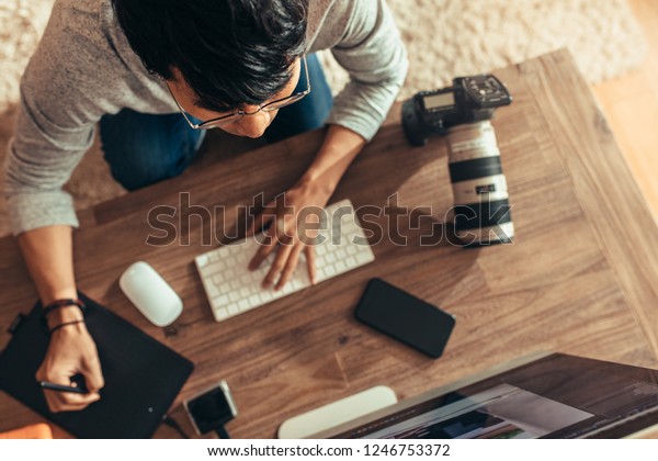 Overhead view of photographer
editing photos at his studio. Photographer editing photos after a
photo shoot using graphic tablet and stylus pen. Focus on
photographer.