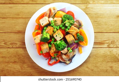 Overhead view of a plate of healthy grilled roast vegetables with tofu, or soybean curd, on a wooden table