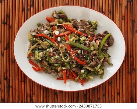 Overhead view of a platter of beef and vegetable stir fry on an oval platter against a brown bamboo place mat