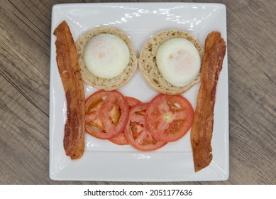 Overhead View Of Poached Eggs Sitting On English Muffin Served With Bacon And Sliced Tomato For A Hearty Breakfast.