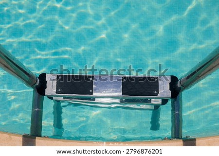Overhead view of pool ladder step with non-slip rubber pads on aluminum frame submerged in clear turquoise pool water, pool ladder step with mosaic tile bottom clearly visible through the water