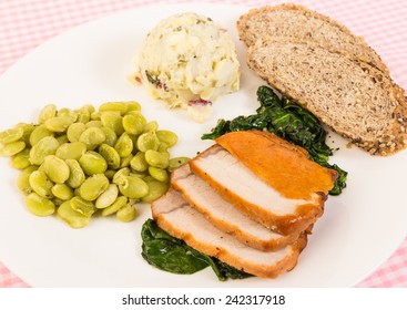 Overhead View Of Pork Tenderloin Roast On Bed Of Wilted Spinach With Potato Salad And Beans.