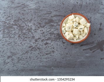 Overhead View Of A Portion Of Crumbled Blue Cheese In A Small Bowl Offset On A Gray Background Illuminated With Natural Lighting.