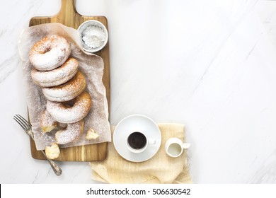 Overhead View Powdered Sugar Doughnuts On Wooden Chopping Board With A Cup Of Espresso On Marble Table Top. Text Space Images.