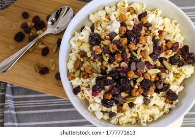 Overhead View Of Rail Mix In A Bowl With Popcorn, Nuts, Chickpeas, Dried Fruit, And Chocolate