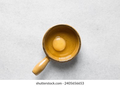 Overhead view of raw egg in a ceramic ramekin, whole raw egg in a ramekin with handle
