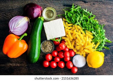 Overhead View of Roasted Veggie Pasta with Feta Ingredients: Feta cheese, vegetables, olive oil, and other raw ingredients on a wood background