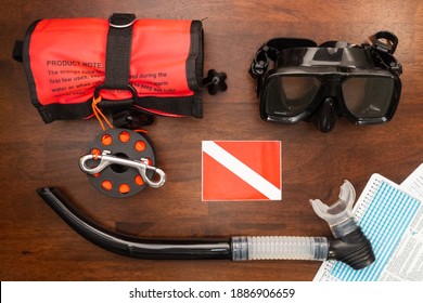 Overhead View Of SCUBA Gear And Equipment Including An Inflatable Tube, Snorkel, Mask, And Dive Table On A Wooden Background