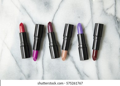 Overhead View Of A Selection Of Bright Lipstick Make Up Arranged On A White Marble Counter Background