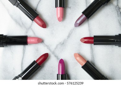 Overhead View Of A Selection Of Lipstick Make Up Arranged In A Circle On A White Marble Counter Background