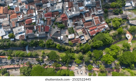 Overhead view showcases a dense residential area alongside a river, framed by trees and pathways - Powered by Shutterstock