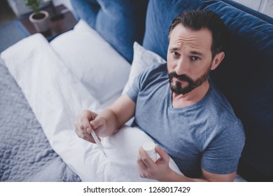 Overhead View Of Of Sick Man Holding At Thermometer Lying In The Bed At Home And Looking At The Camera