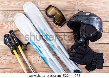 Overhead view of ski accessories placed on rustic wooden table. Items included helmet, goggles, gloves, ski and sticks. Winter sport leisure time concept.