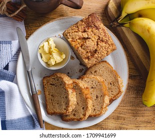 Overhead View Of Sliced Banana Nut Loaf Cake And Butter On A Plate With A Bunch Of Bananas