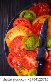 Overhead view of sliced tomatoes on dark wooden surface with knife. Natural seasonal vegetables, healthy cooking concept