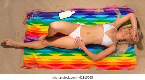 Overhead View Of A Slim Blonde Woman In A White Bikini Lying On A Colorful Beach Towel Sunbathing.