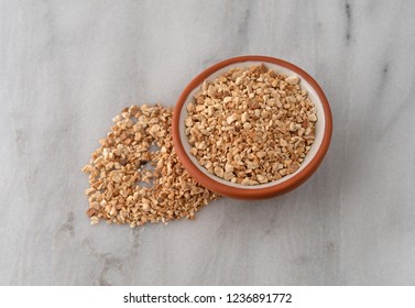 Overhead View Of A Small Bowl Of Cut Orris Root With Spilled Herb To The Side On A Gray Marble Counter Top.