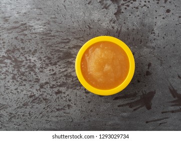 Overhead View Of A Small Yellow Bowl Filled With Applesauce On A Gray Background.