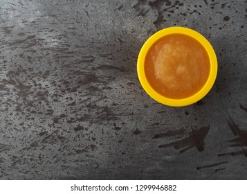Overhead View Of A Small Yellow Bowl Filled With Applesauce Offset On A Gray Background.