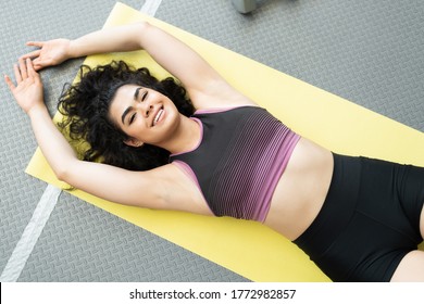 Overhead View Of Smiling Latin Young Woman Exercising On Exercise Mat At Health Club