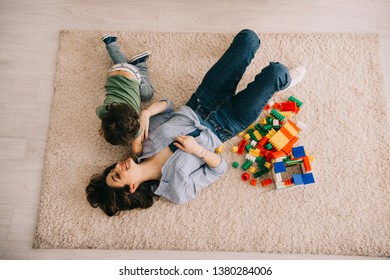 Overhead View Of Smiling Mom And Son Lying On Carpet With Toy Blocks